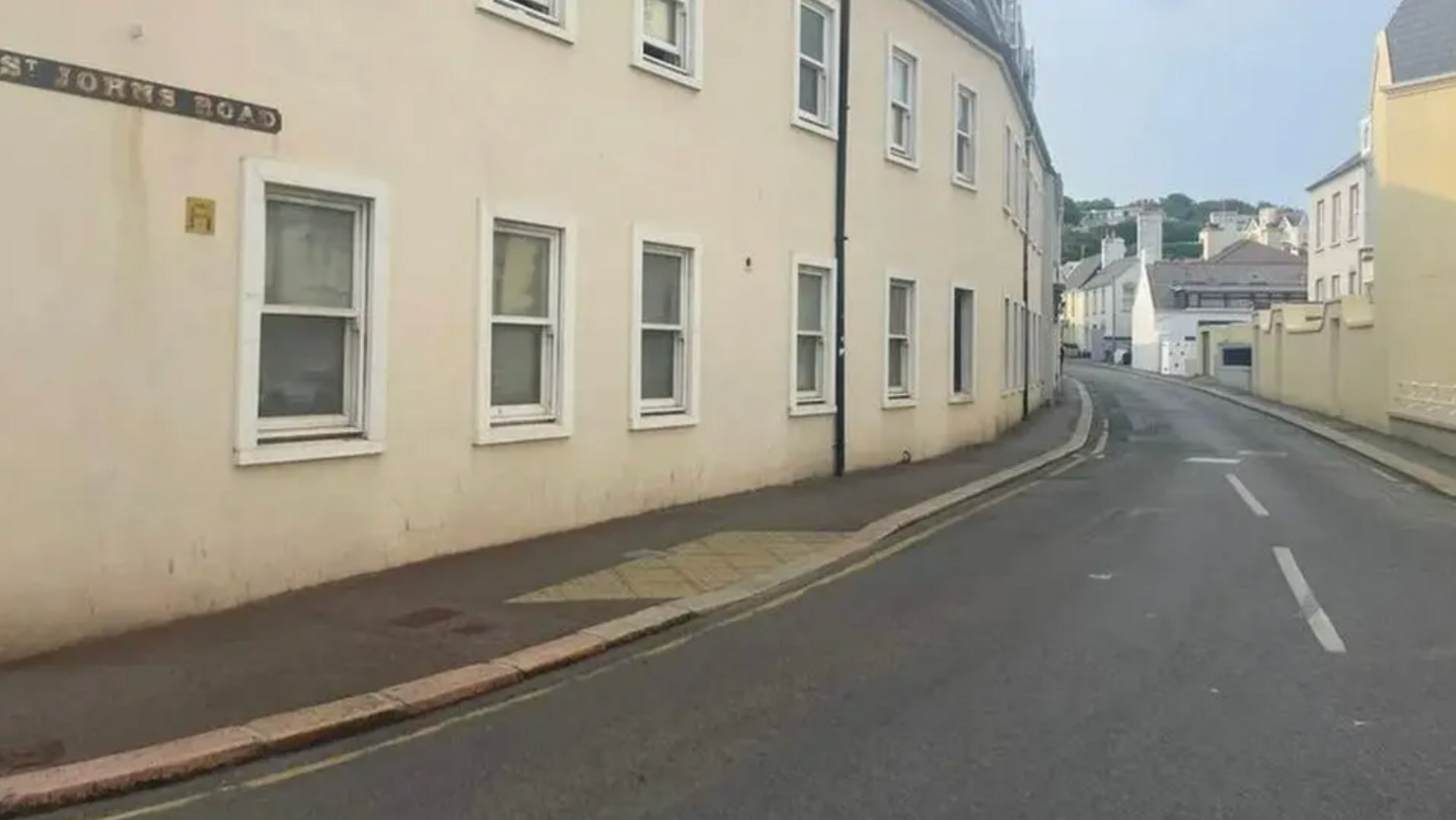 A view of St John's Road. There is a long row of houses on either side. The houses have several street level windows facing towards the street. 