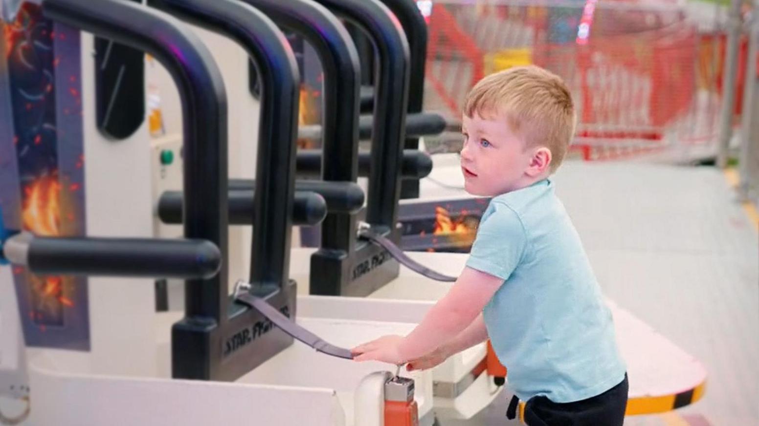 A young boy with ginger hair plugs in a seatbelt on a funfair ride