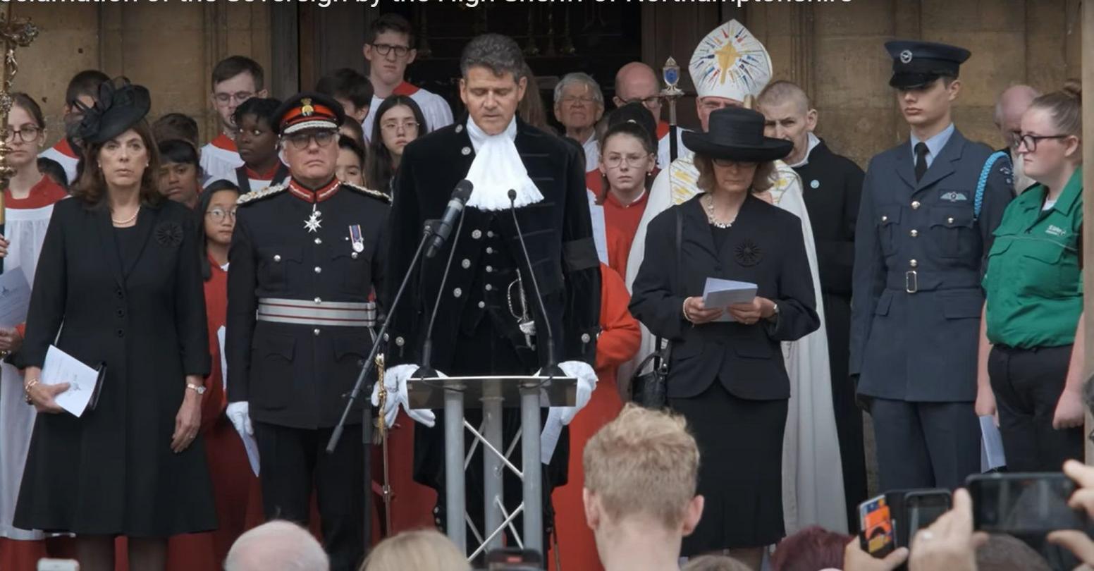 Crispin Holborow in ceremonial black uniform with lace at the collar and cuffs making an announcement