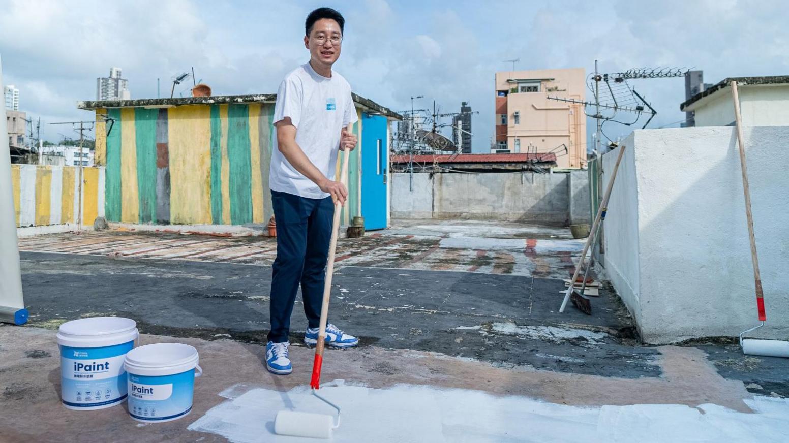 Martin Zhu painting the flat roof of a building with a long-handled roller and his firm's white paint.