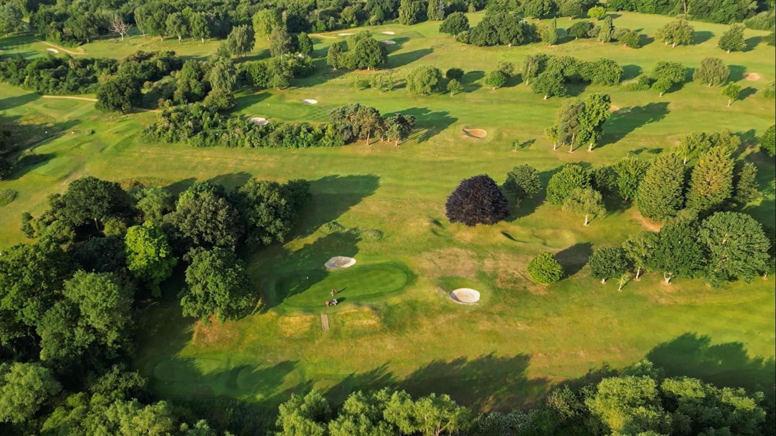 An aerial shot of Oxford Golf Club. The greens are well kept, and there are large sections of fairway. There are trees across the course.