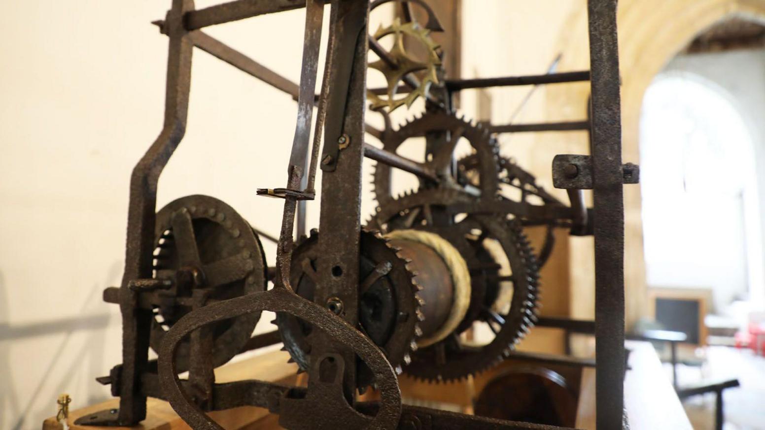 The wrought iron frame of the device houses cogs attached to a winding mechanism.
