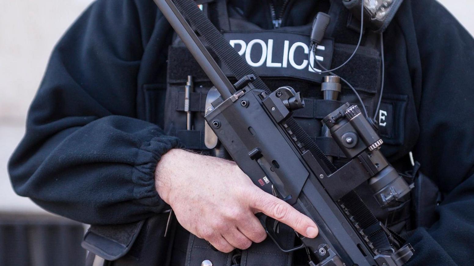 A close-in shot of an armed police officer in uniform, holding a gun