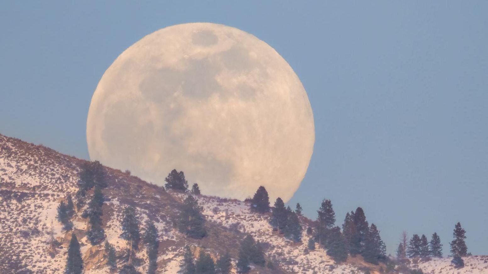 February's full moon also known as Snow Moon rises over Boise Idaho sky in the evening of late winter season.