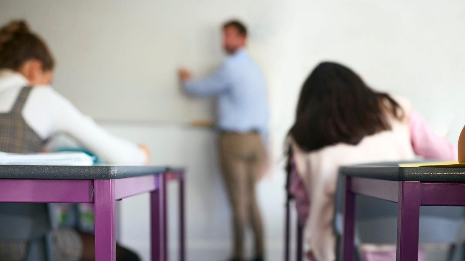 Teacher at the front of the classroom teaching two students. 