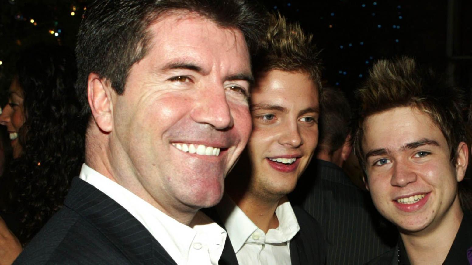 Simon Cowell, Mark Rhodes and Sam Nixon standing together and smiling at the camera during an event.