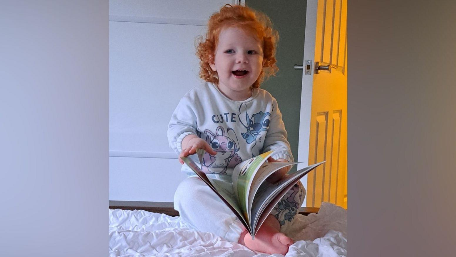 Niamh reading a book. She has red curly hair, wearing grey Lilo and Stitch pyjamas.