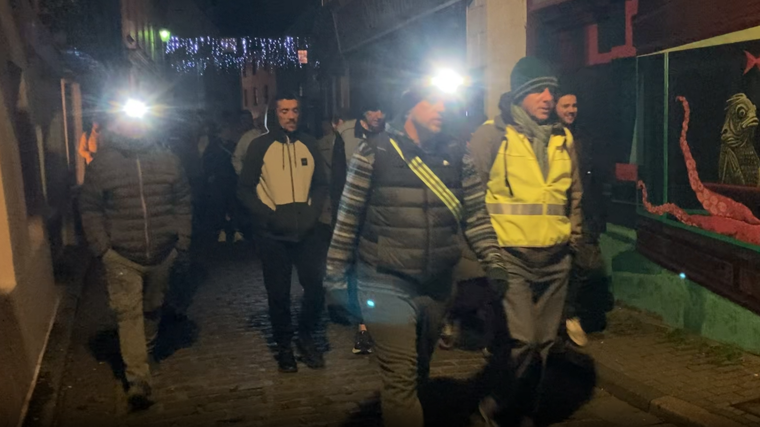 A group of men pictured walking in high vis jackets and head torches.
