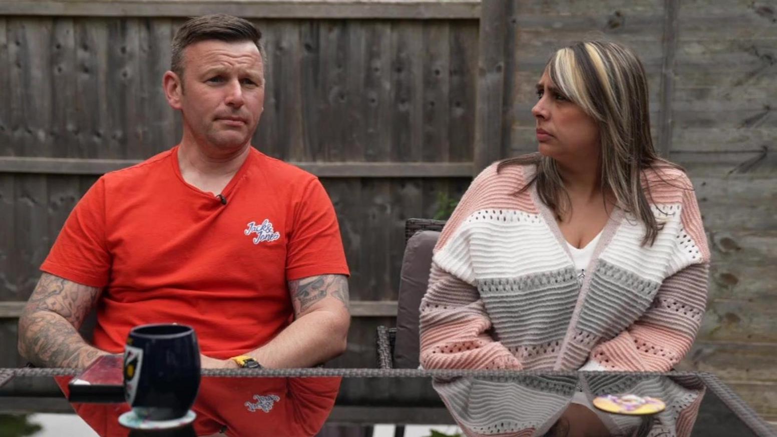 Peter Felix sits at a table in his garden with his partner Rebecca Wilson. Both have worried expressions.