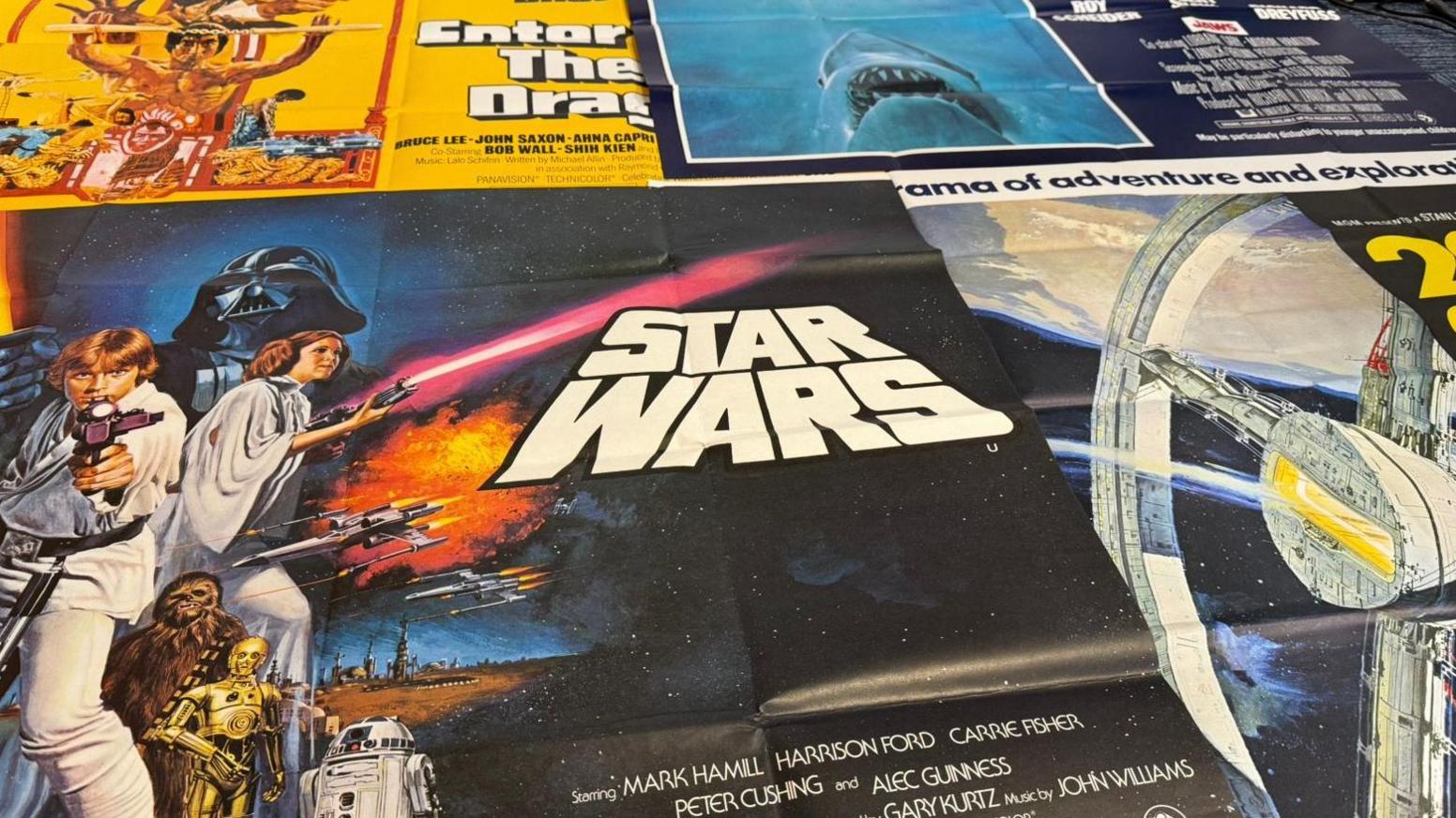 The picture shows a collection of 40 x 30 inch film posters. The one on the left hand side, in the foreground, is Star Wars. At the top of the photo is an Enter the Dragon poster, and a Jaws poster.