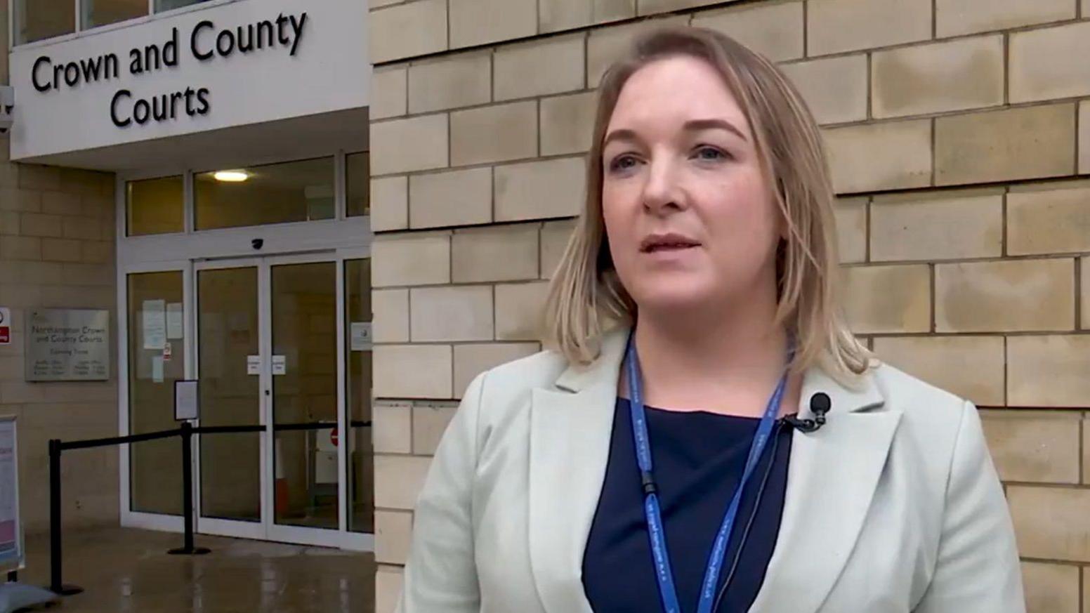 Det Ch Insp Liz Basham with medium-length blond hair wearing a cream-coloured jacket, black top and blue lanyard outside a stone-built court building.