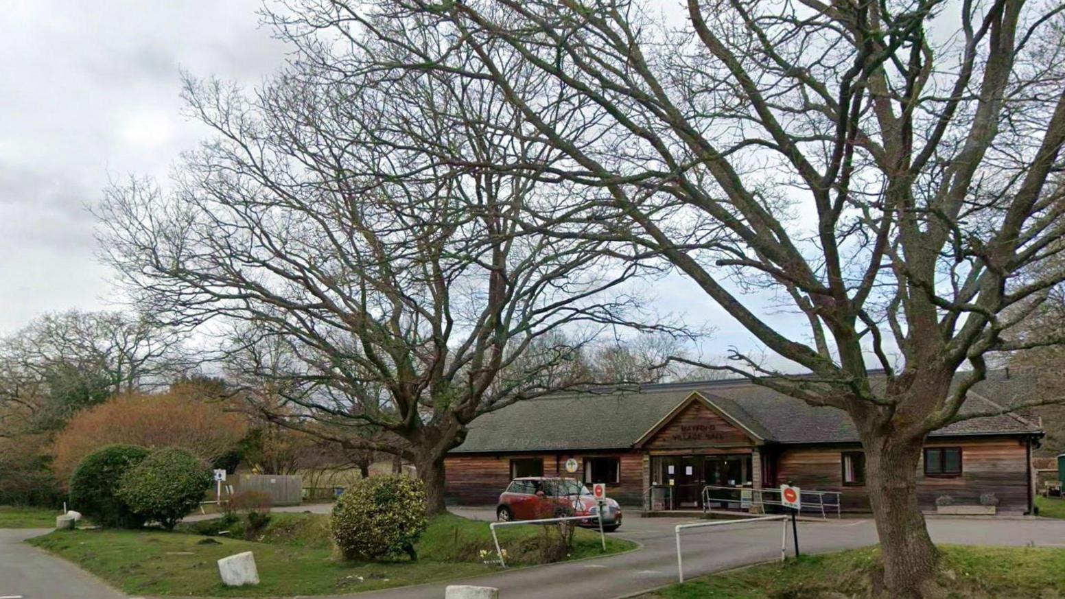 A house surrounded by bare winter trees under a grey, cloudy sky. 