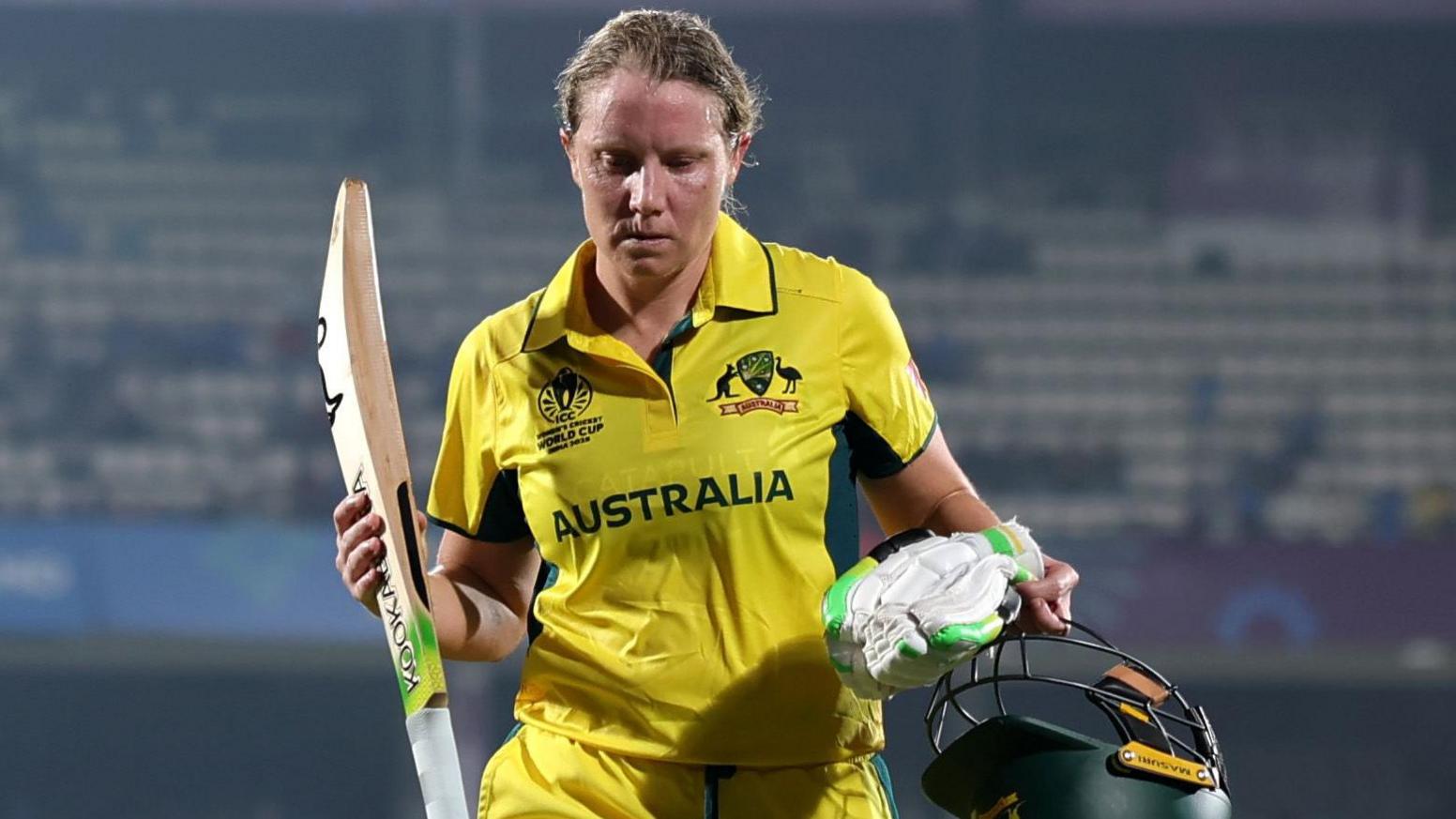 Alyssa Healy walks off the pitch holding her bat, helmet and gloves
