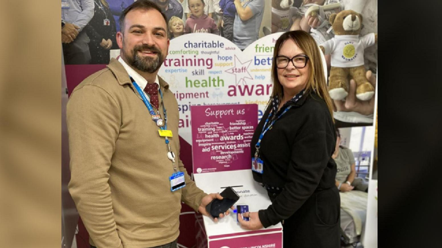 Ben wears a mustard colour jumper and has a beard, and Dawn is smartly dressed and wears glasses. The donation point is a cardboard post box, and they are holding their phone and credit cards next to it.