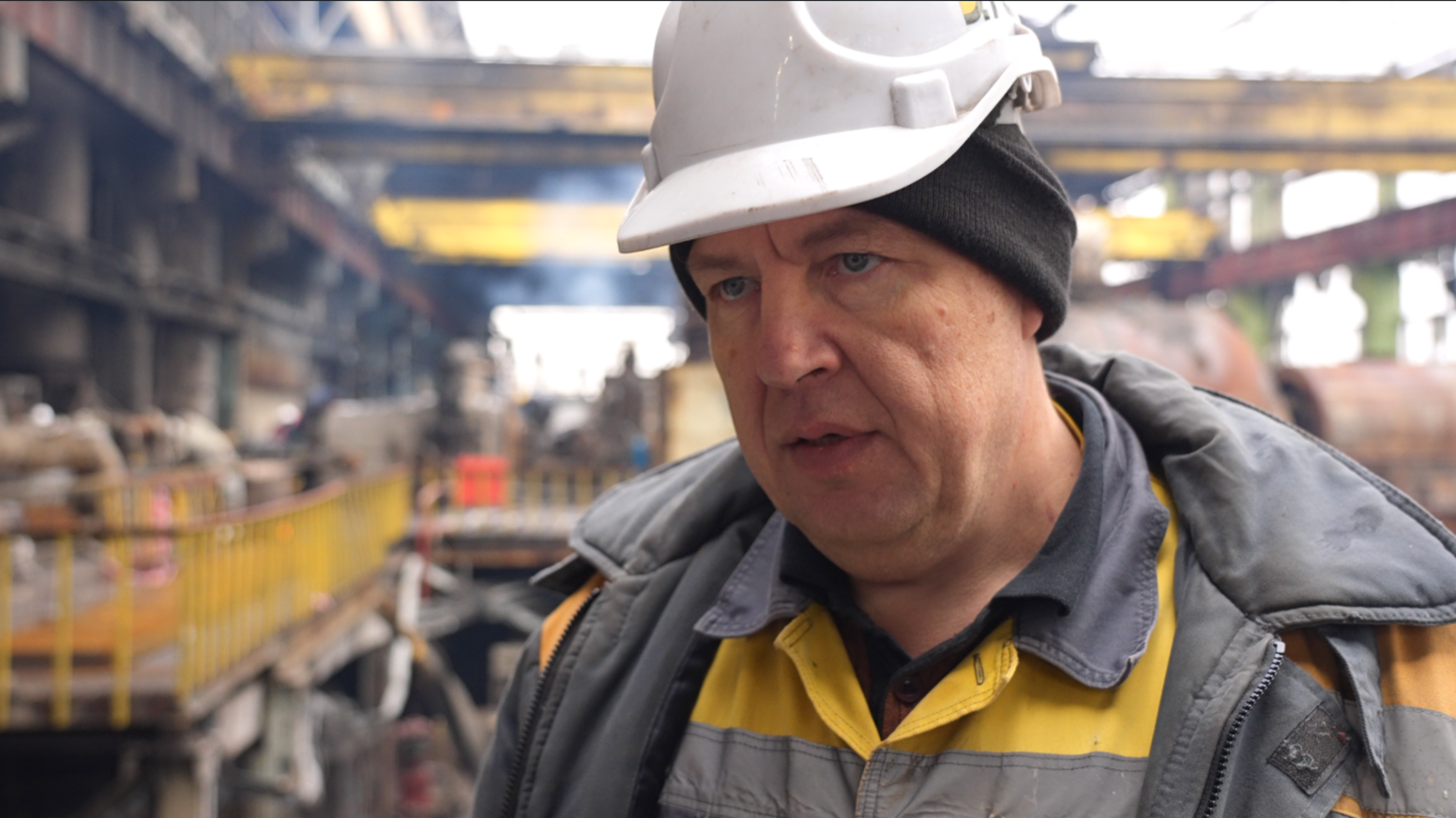 Oleksandr - he is wearing a white safety helmet on top of a black beanie hat. He is looking towards the camera