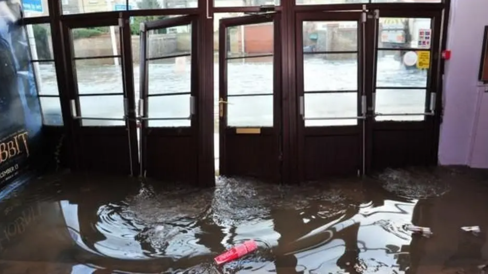 Flood water covers the floor at the entrance to a cinema in Lowestoft. The four brown doors which lead to the inside and outside of the building have been dislodged slightly by the flooding.