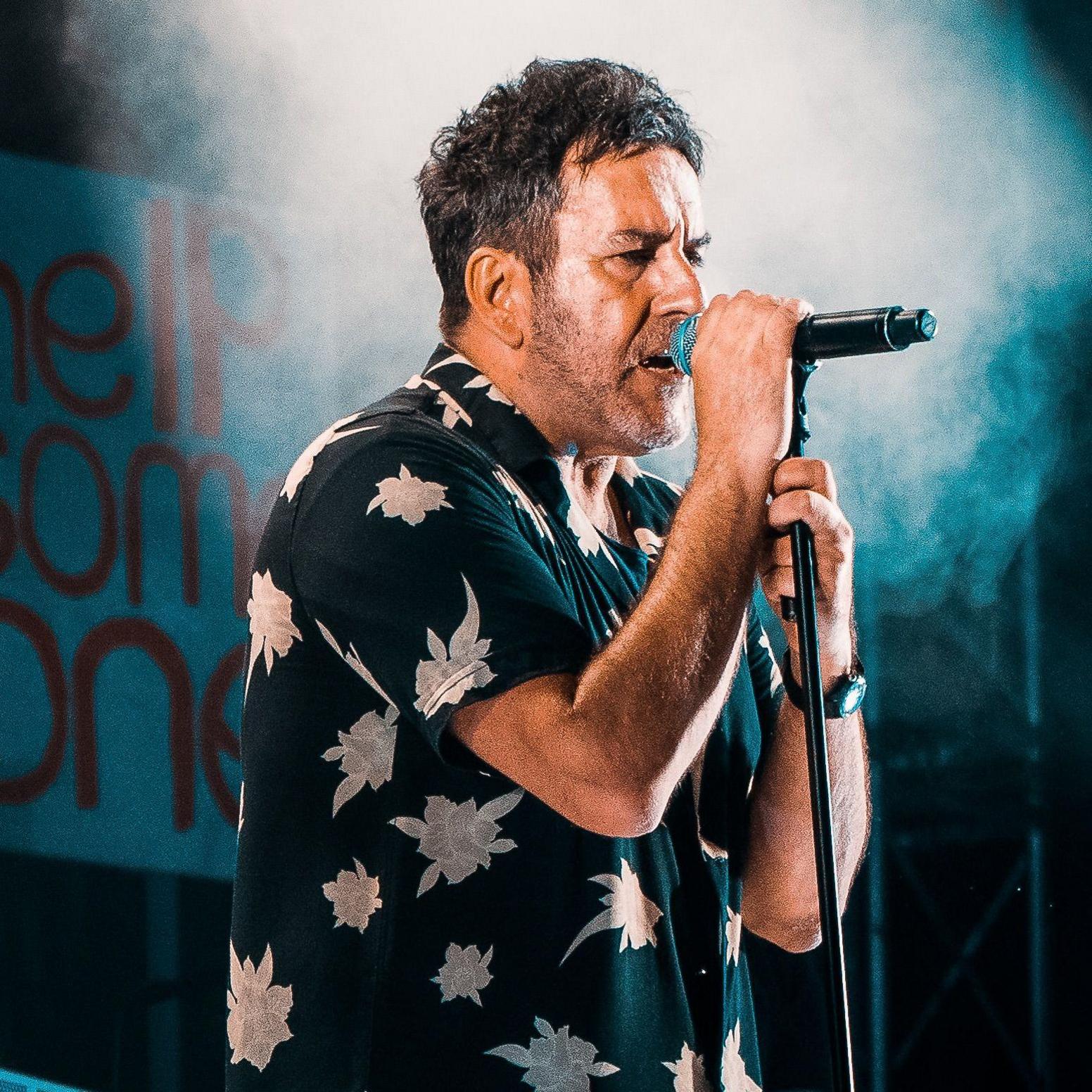 Terry Hall is wearing a dark shirt with white flowers on it. He is singing into a microphone during the 2019 concert at Coventry Cathedral 