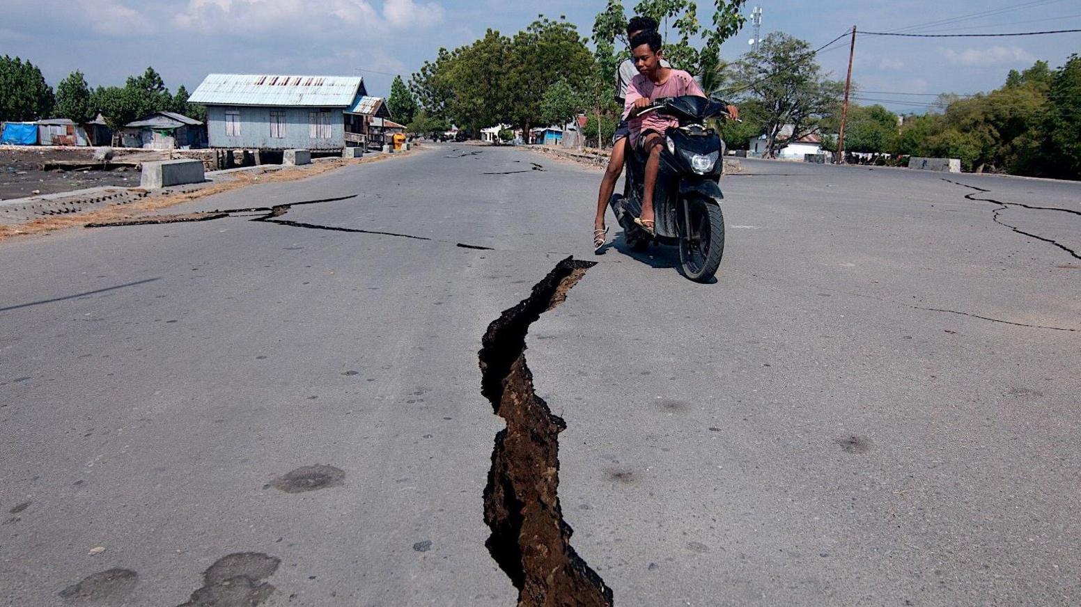 A motorcyclist rides past a crack on the road following the earthquake in East Nusa Tenggara Province, Indonesia