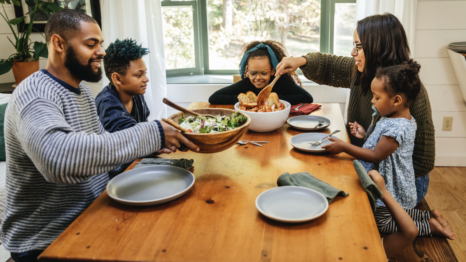 Family of five sat around table eating salad and garlic bread