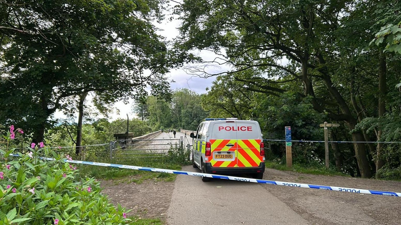 Police van in front of bridge with police tape behind it