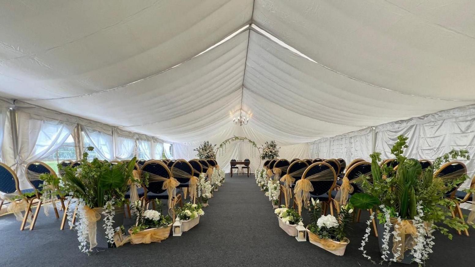 A marquee set out as a wedding venue with chairs and flowers