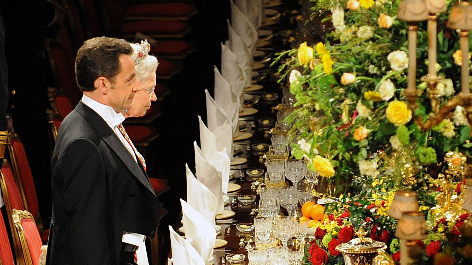 Queen Elizabeth and Nicolas Sarkozy at a grand state dinner in 2008, surrounded by flowers.