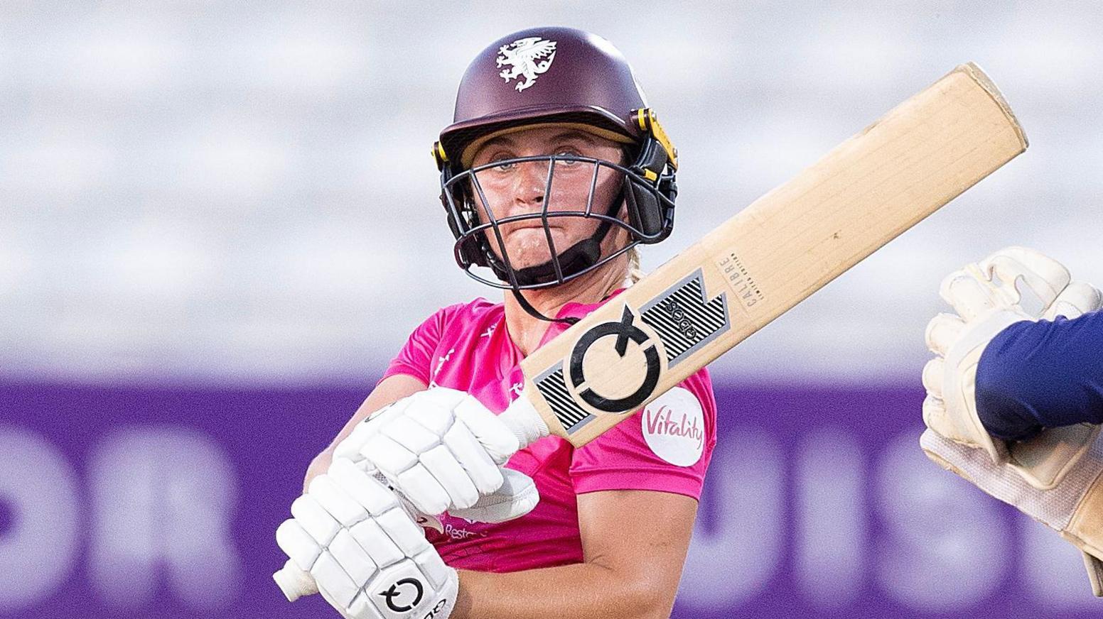 Niamh Holland in a pink shirt swipes her bat
