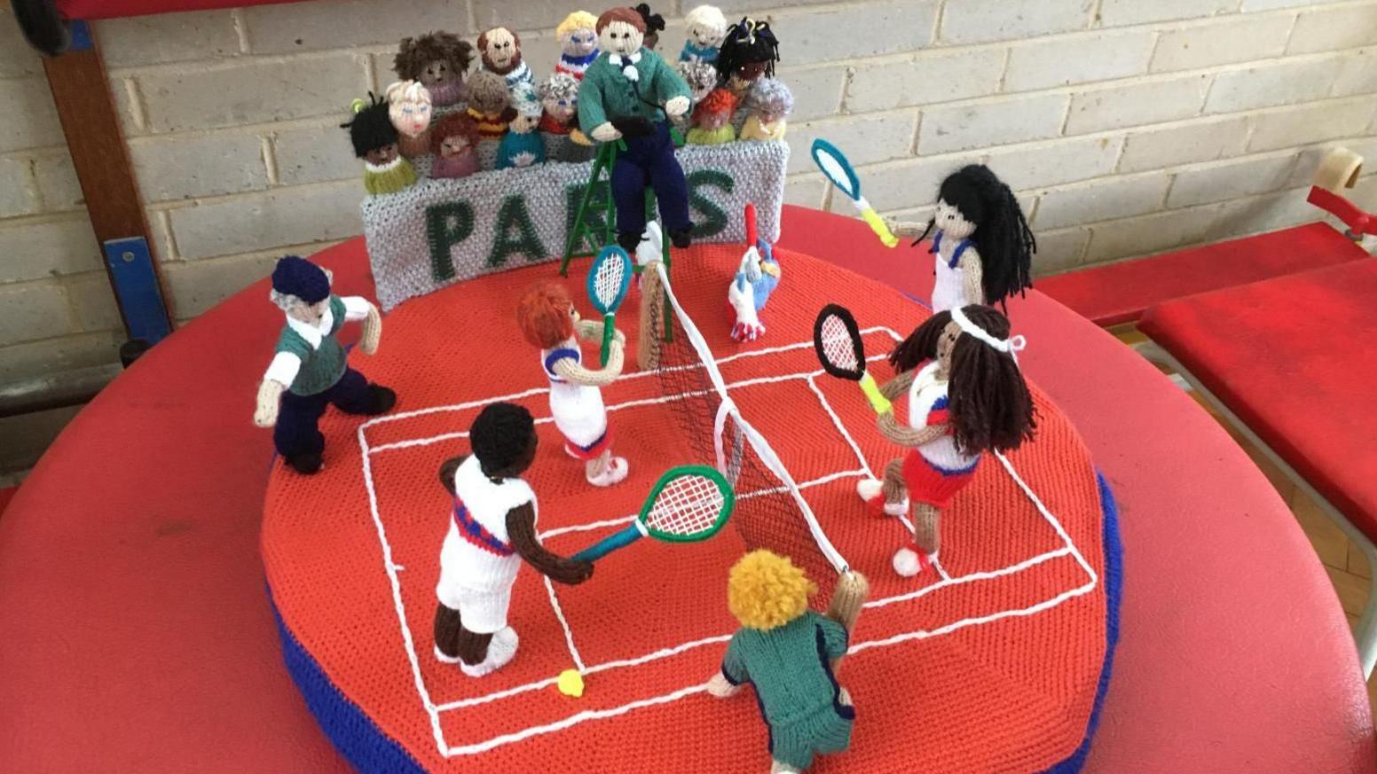 Knitted tennis players play in front of a crowd of spectators, with 'Paris' written in the stand