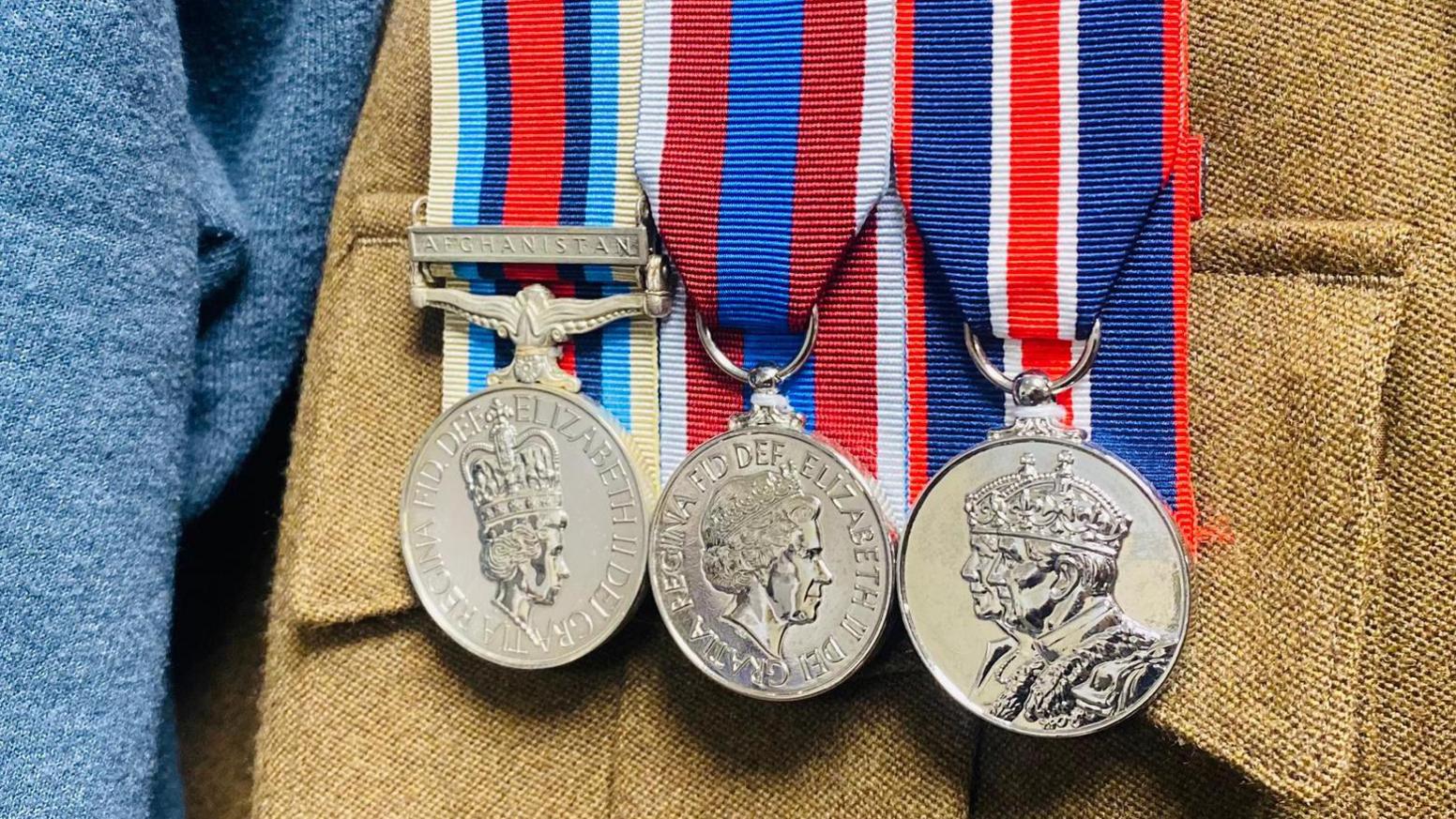 Three silver, coin-shaped medals hanging from ribbons