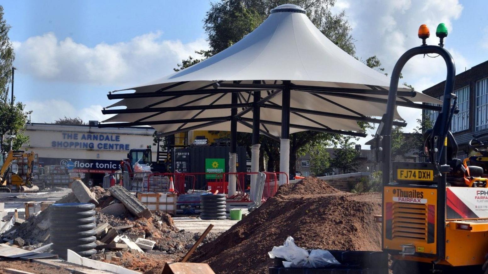 Shipley's market square with a new white canopy in the middle of the image surrounded by contractors' vehicles, rubble and piles of soil