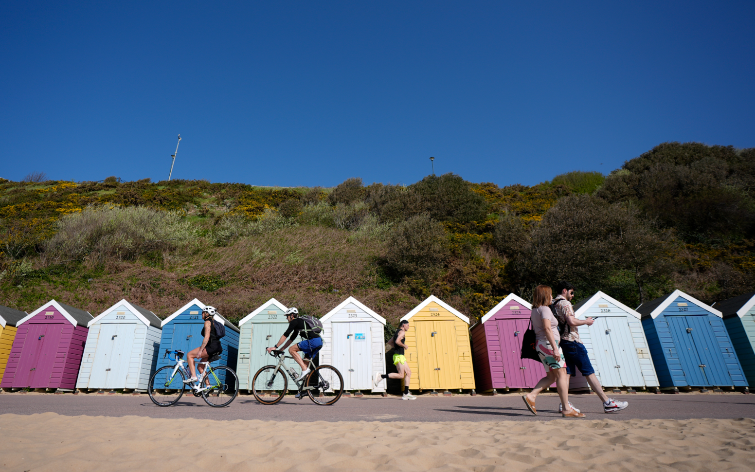 People make their way past beach huts on Bournemouth beach in Dorset.