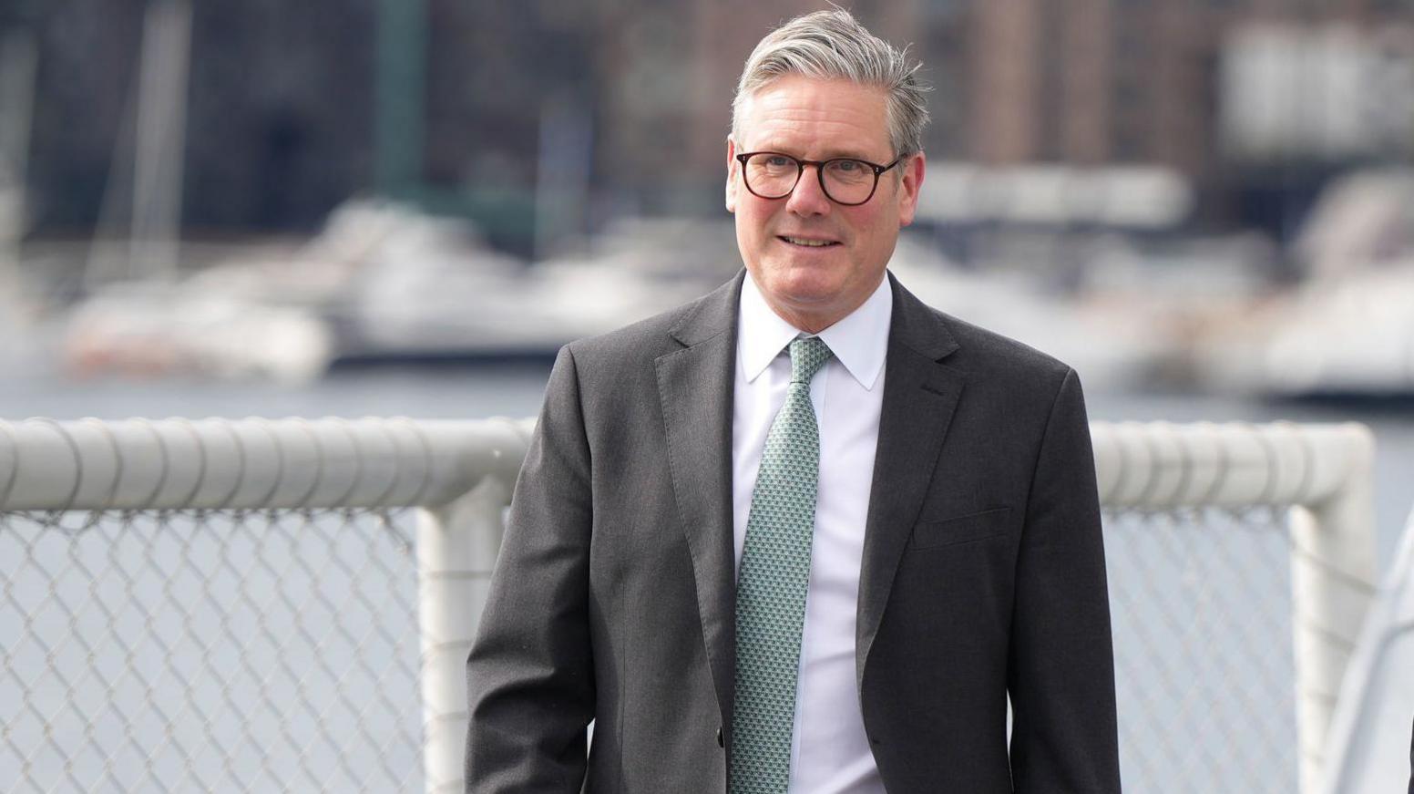 Sir Keir Starmer, wearing a dark suit and grey/green tie, walking on a ship deck of a Norwegian coast guard vessel