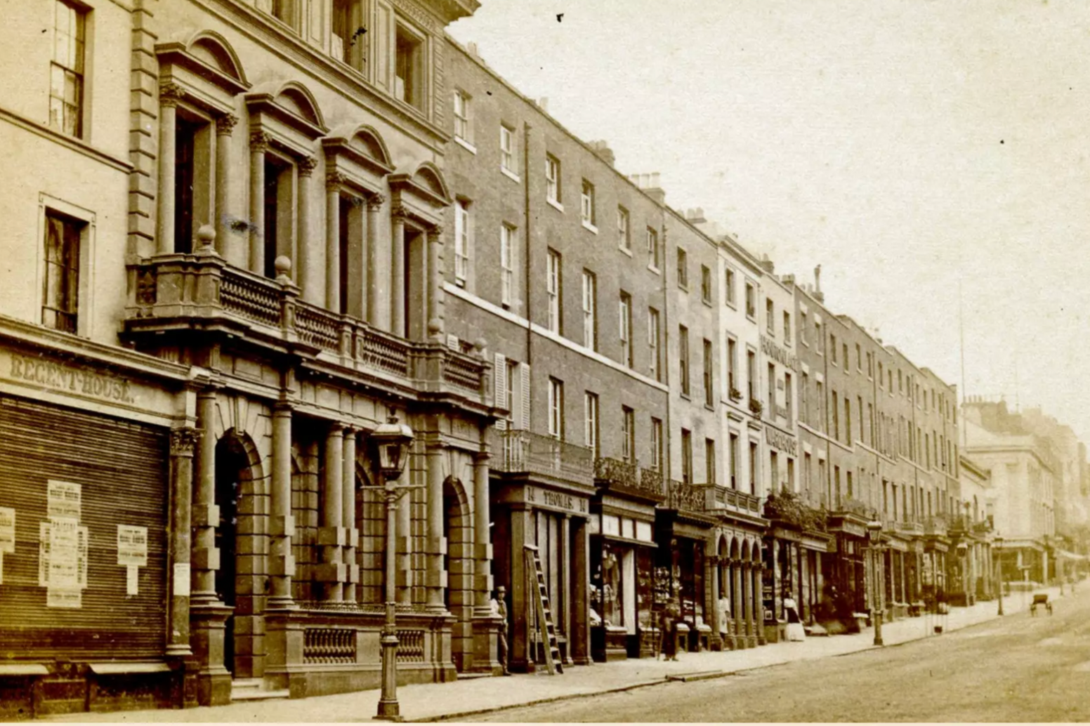A sepia image of Leamington Spa's Upper Parade pictured in 1861. Rows of terraced buildings stand along a road with wrought iron lamp-posts in front of them.