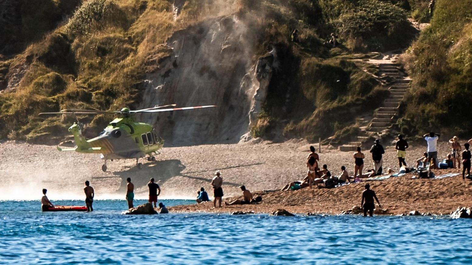 An air ambulance helicopter on a beach. In the foreground are lots of people watching