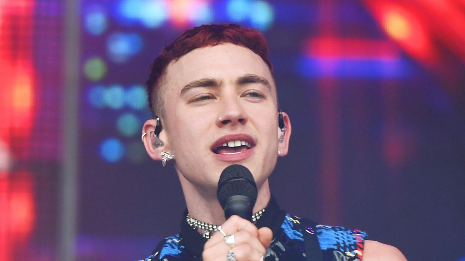 Olly Alexander performing into a microphone on stage at Glastonbury