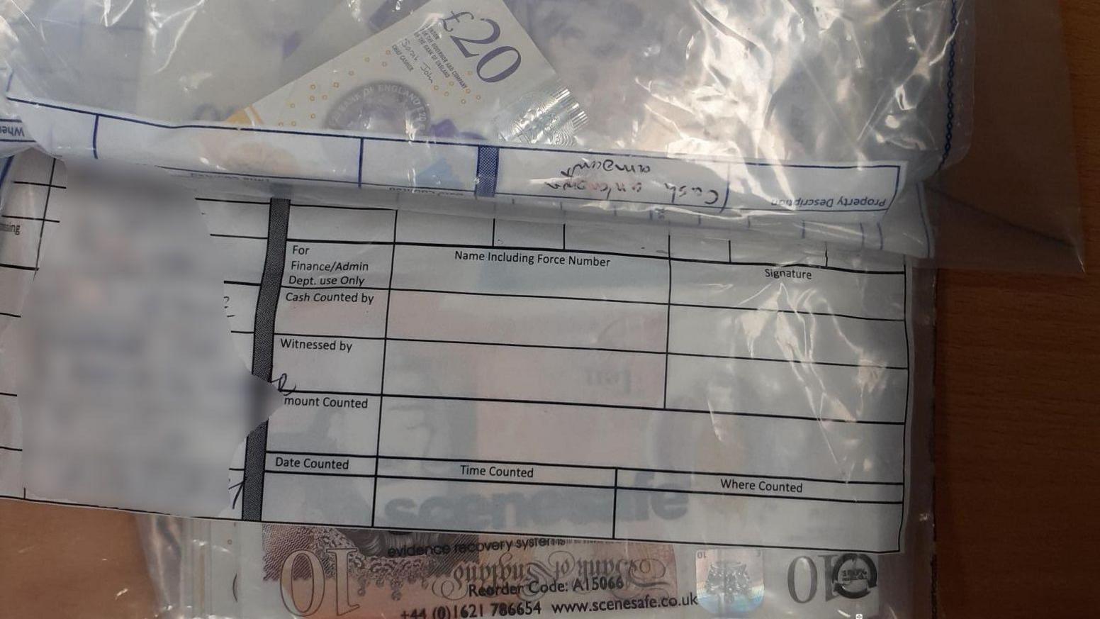 £10 and £20 notes are seen inside a police evidence bag laid on a wooden table. 