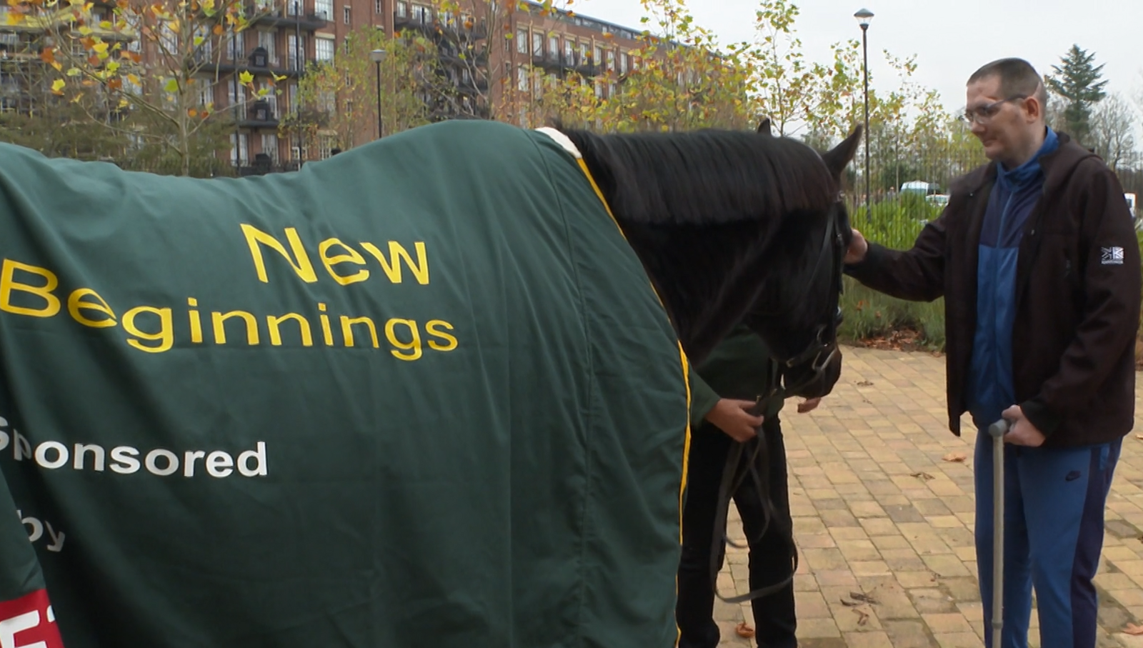 A resident of Brainkind interacting with Remy at the clinic in York. The dark horse is covered with a green covering with the words "New Beginnings" on the side. 