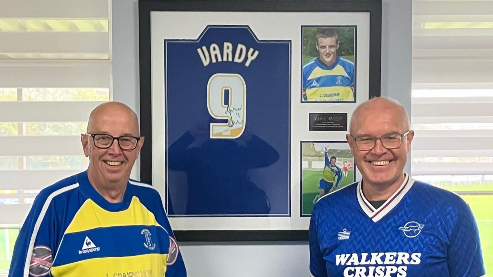 Two men stood in front of a framed Jamie Vardy shirt, which also has pictures of the forward