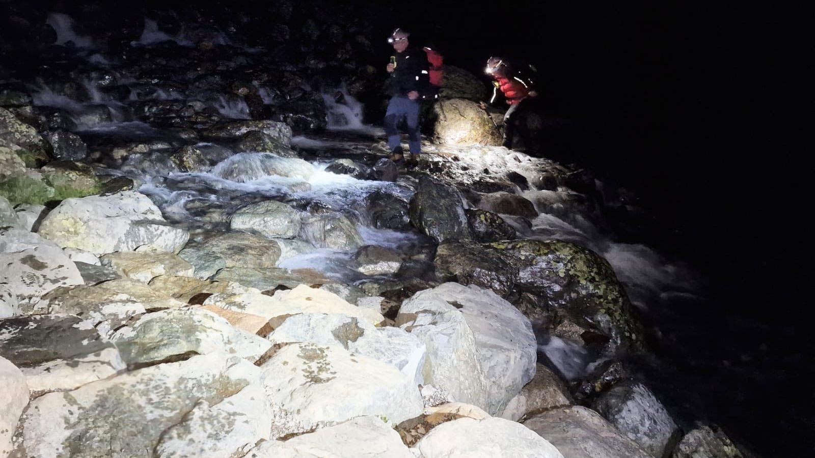 Mountain Rescue volunteers, wearing head torches and emergency gear, walk over a swollen waterway which crosses a path. The two members were deployed in the search for a young walker.
