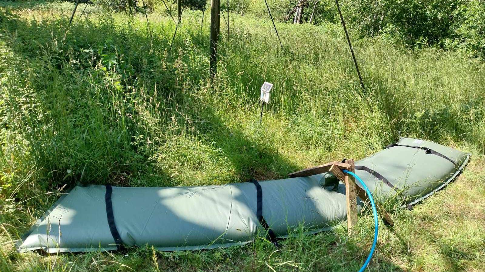A large green bag in the grass with a hosepipe going into it