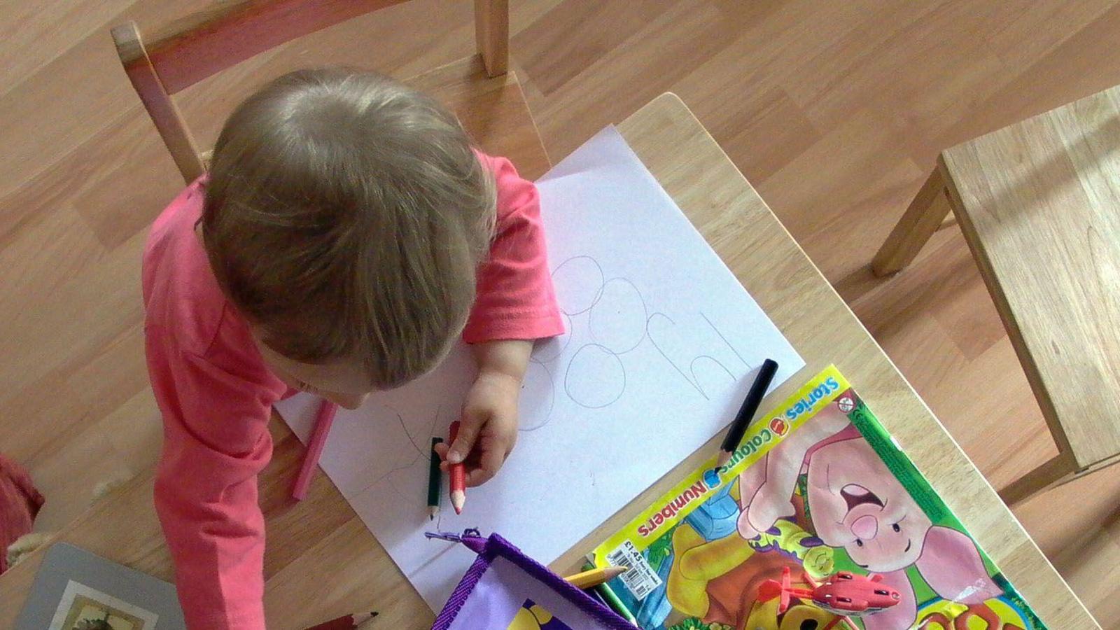 A small child draws on a piece of paper with crayons