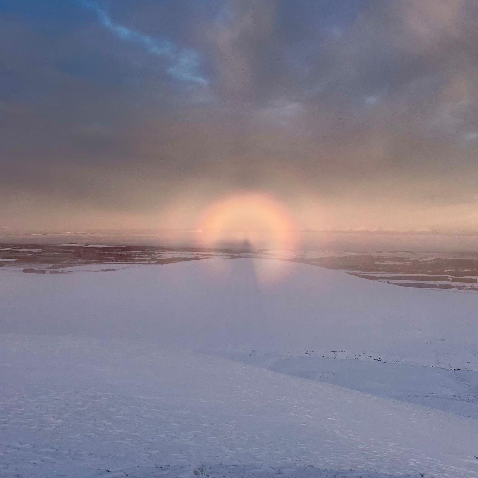 The Brocken spectre appears as a large shadowy figure with a bright halo. The hilltop is covered in snow.