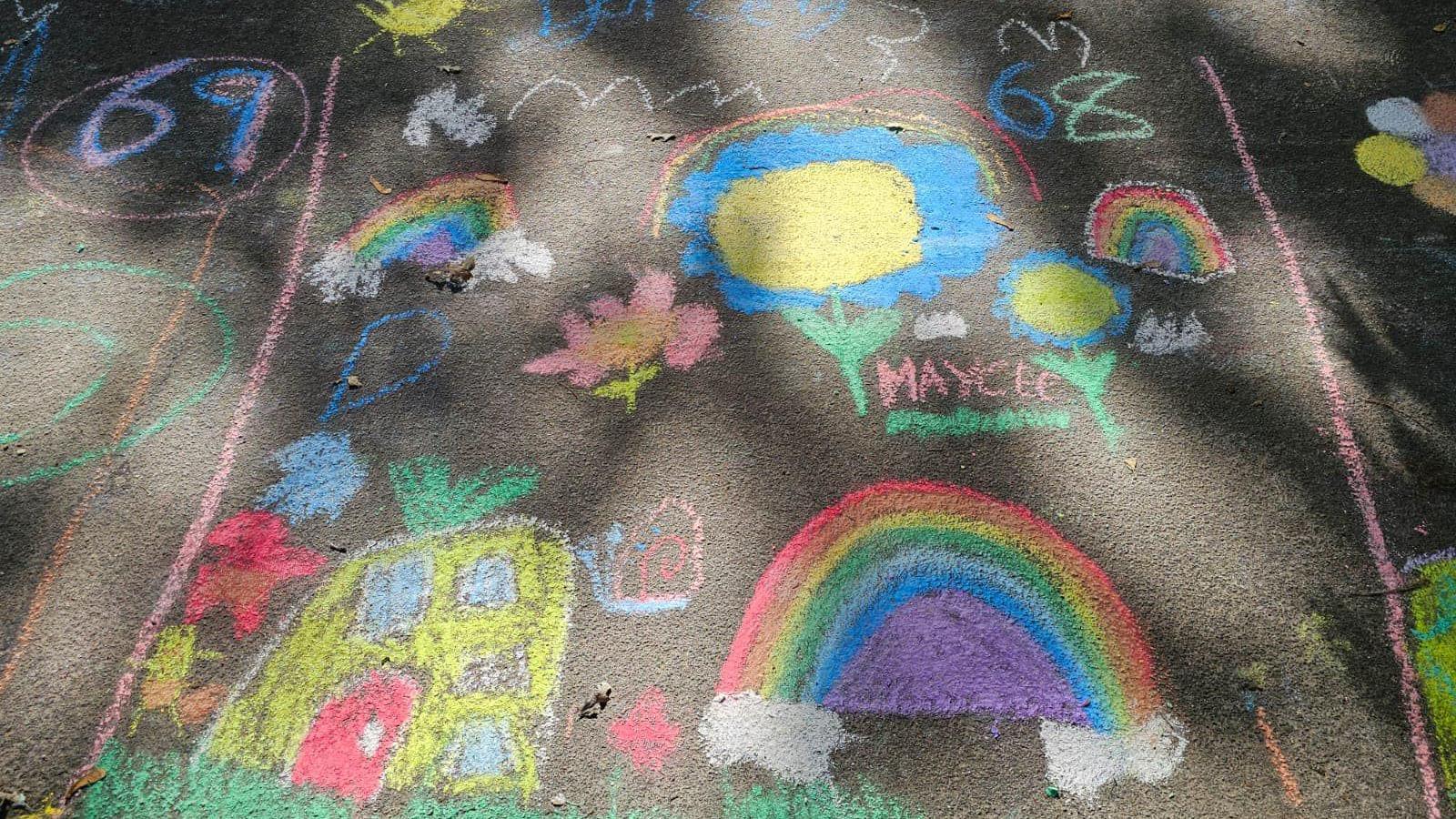 Art work on the tarmac drawn in chalk - a pineapple house depicting spongebob squarepants characters bottom left, a rainbow bottom right, another smaller rainbow, flowers and a cloud top left and bigger blue flowers and the name Maycee next to another rainbow top right