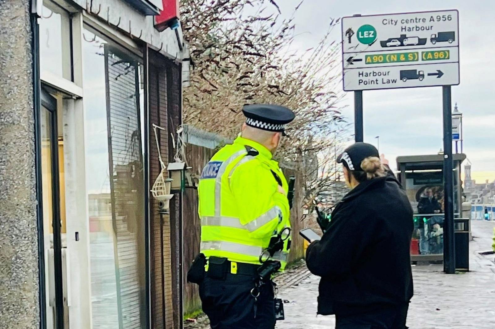 Two police officers on street, one in a hi-vis yellow jacket, the other in dark clothing, with a road sign in background showing directions for harbour traffic.