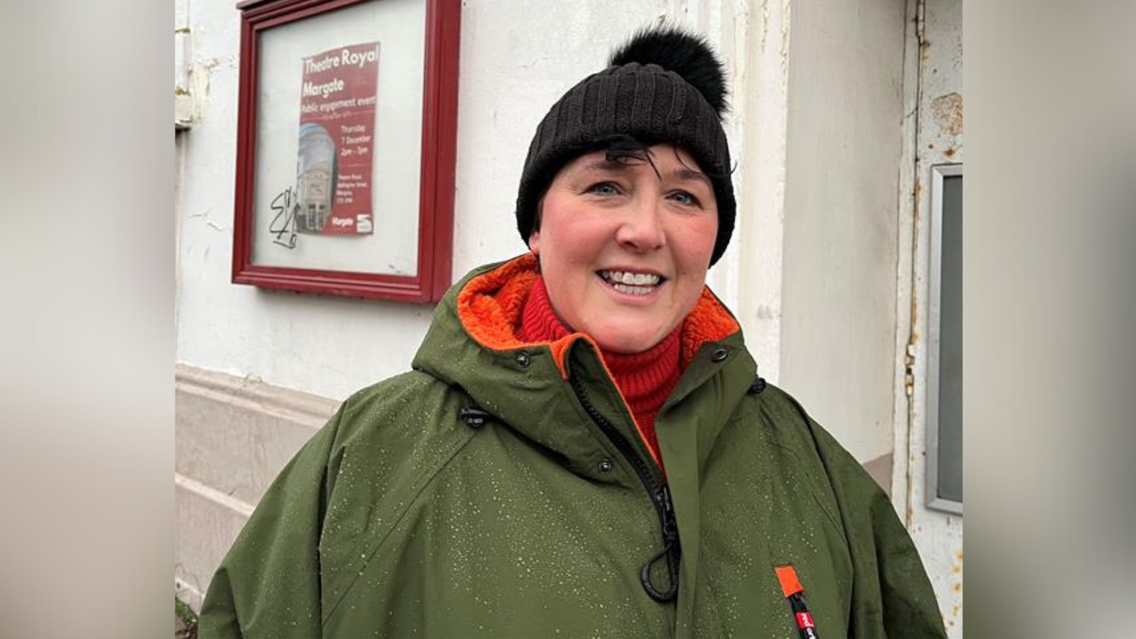 Sinead Schaverien from Margate. She is wearing a green dry-robe and a black bobble hat. She is stood outside the Theatre Royal in the town.