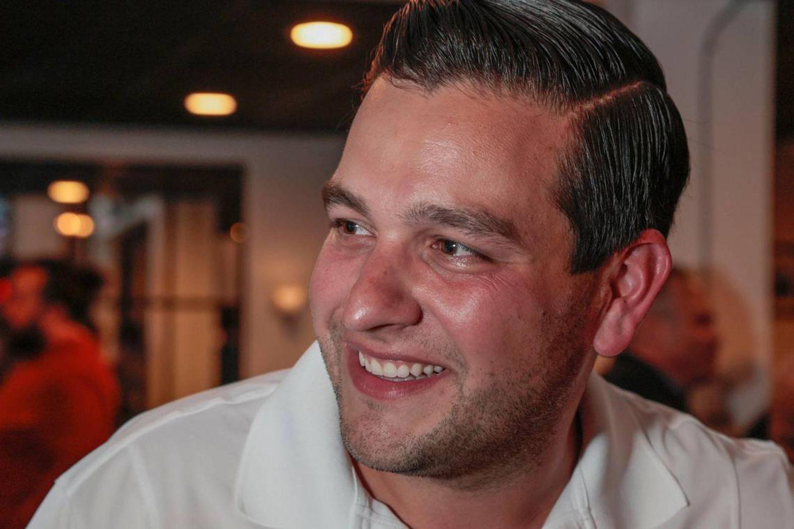 A man in a white shirt smiles, with his face pointed away from the camera