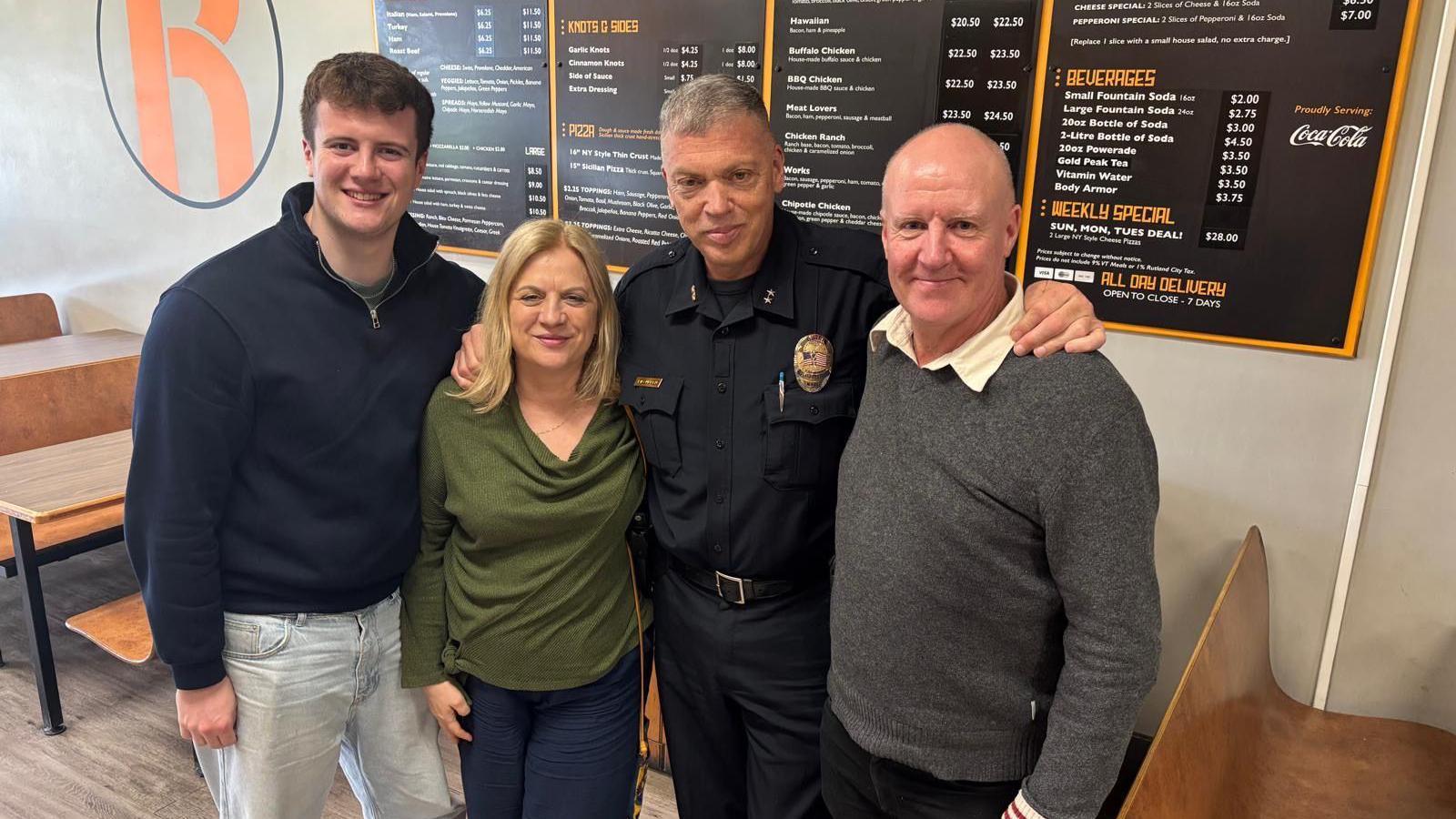 Three men and one woman standing in front of a menu board in a restaurant