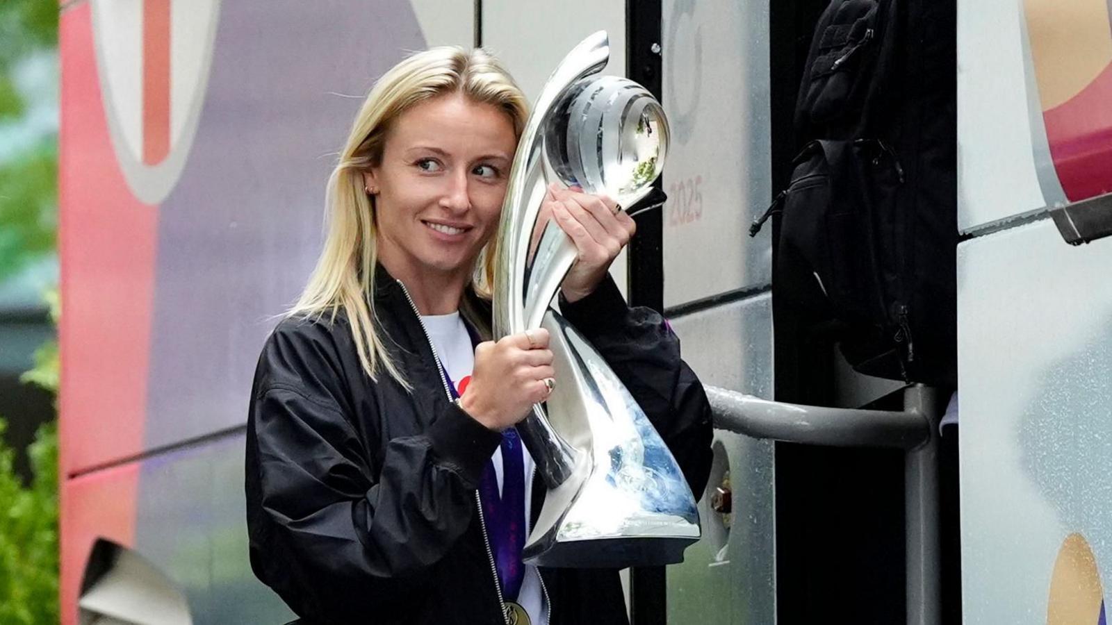 Leah Williamson getting on the England team bus holding the Euros trophy