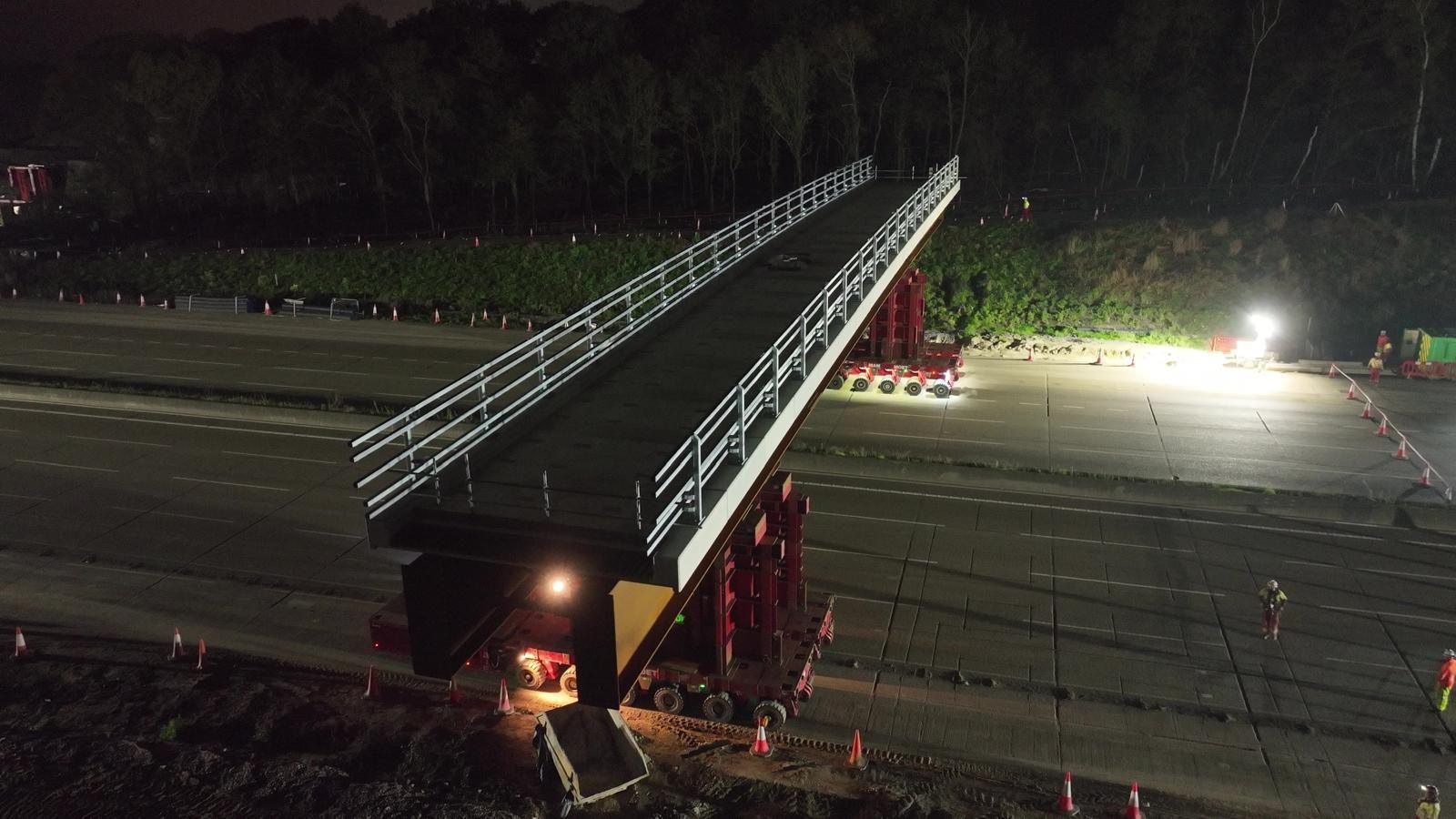 Workers install the new Clearmount bridge across the road at night