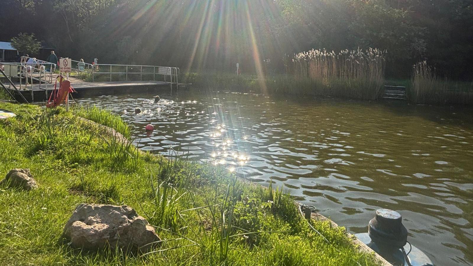The sunshine glints on the water at Henleaze Lake in Bristol as swimmers paddle in the distance